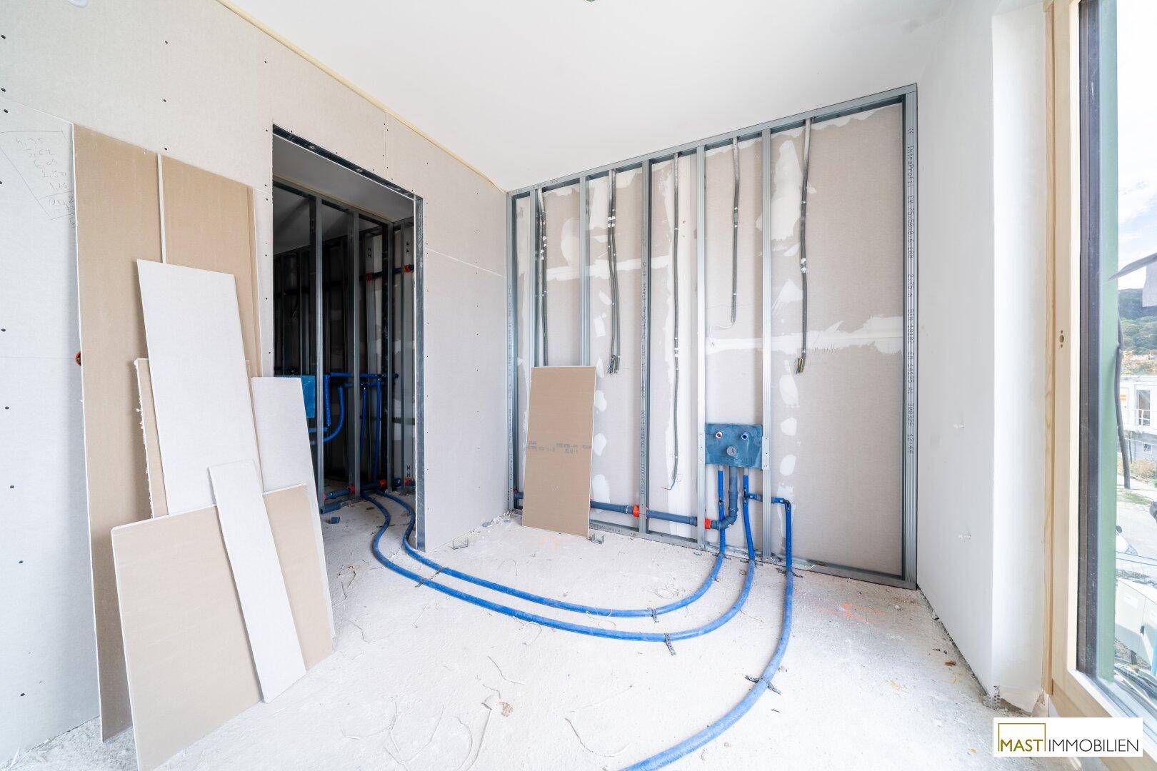 Rohbau-Raum mit Metallständerwerk und umfangreichen Sanitärinstallationen, bereit für den weiteren Ausbau.