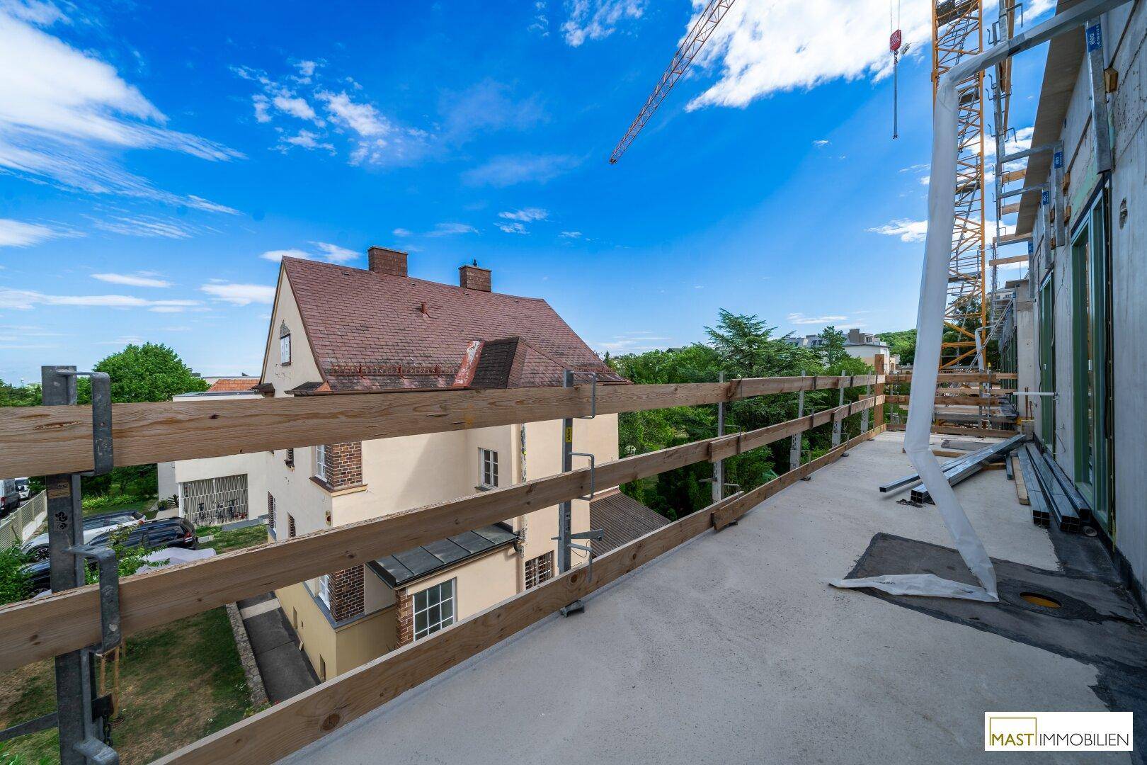 Im Bau befindlicher Balkon mit Holzsicherheitsgeländer und Blick auf ein charmantes Altbauhaus.