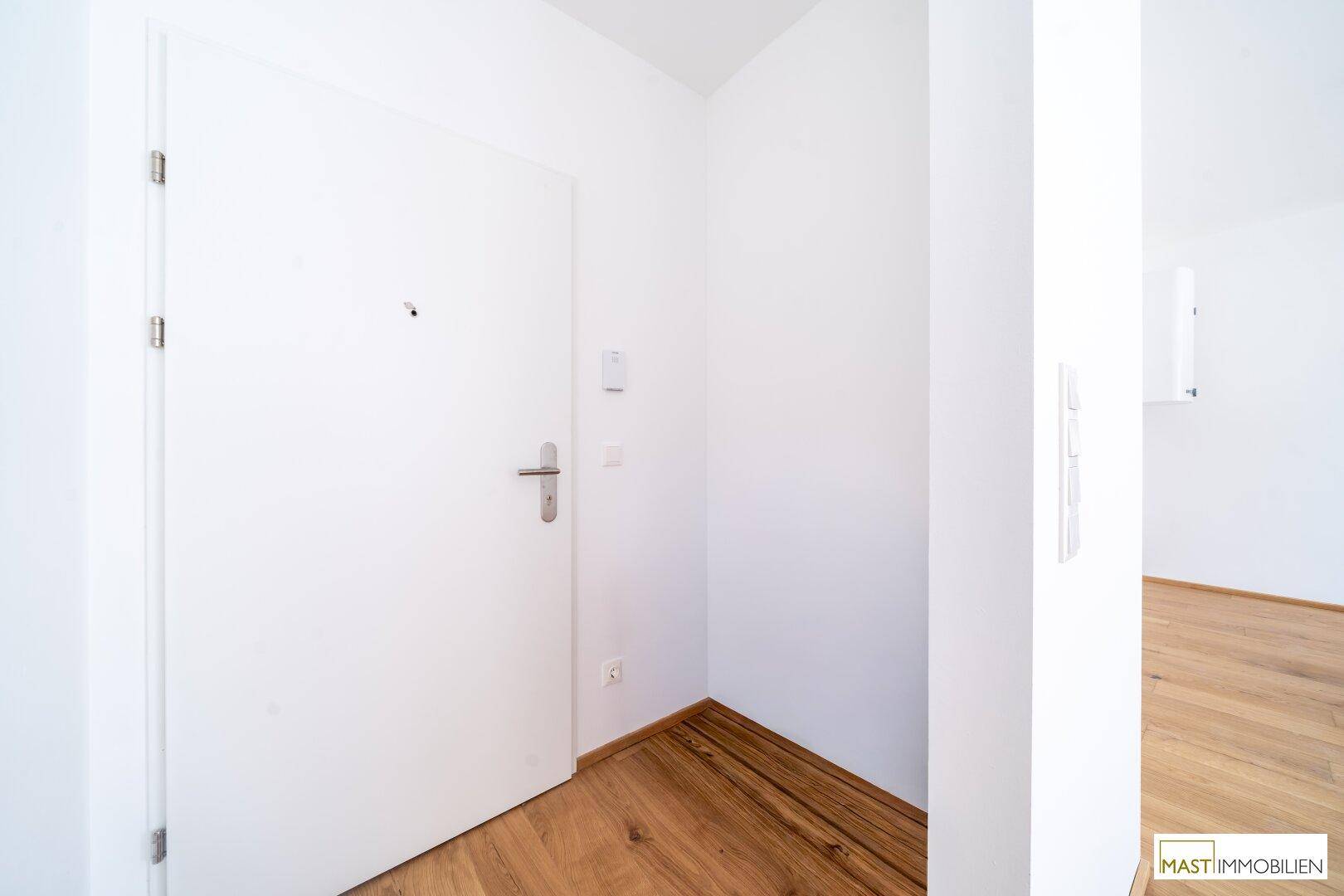 Eingangsbereich mit weißer Tür und Holzboden, der einen sauberen und modernen ersten Eindruck vermittelt.