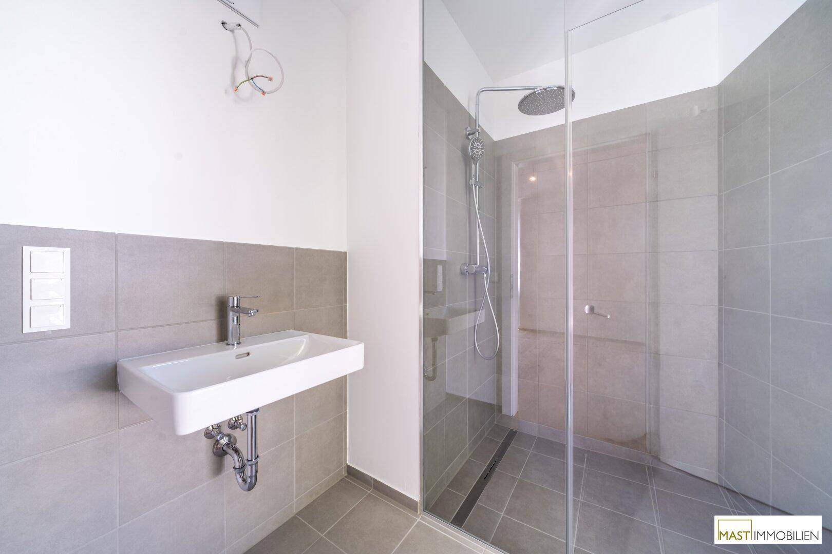 Zeitgemäßes Badezimmer mit wandhängendem Waschbecken und geräumiger, ebenerdiger Dusche.
