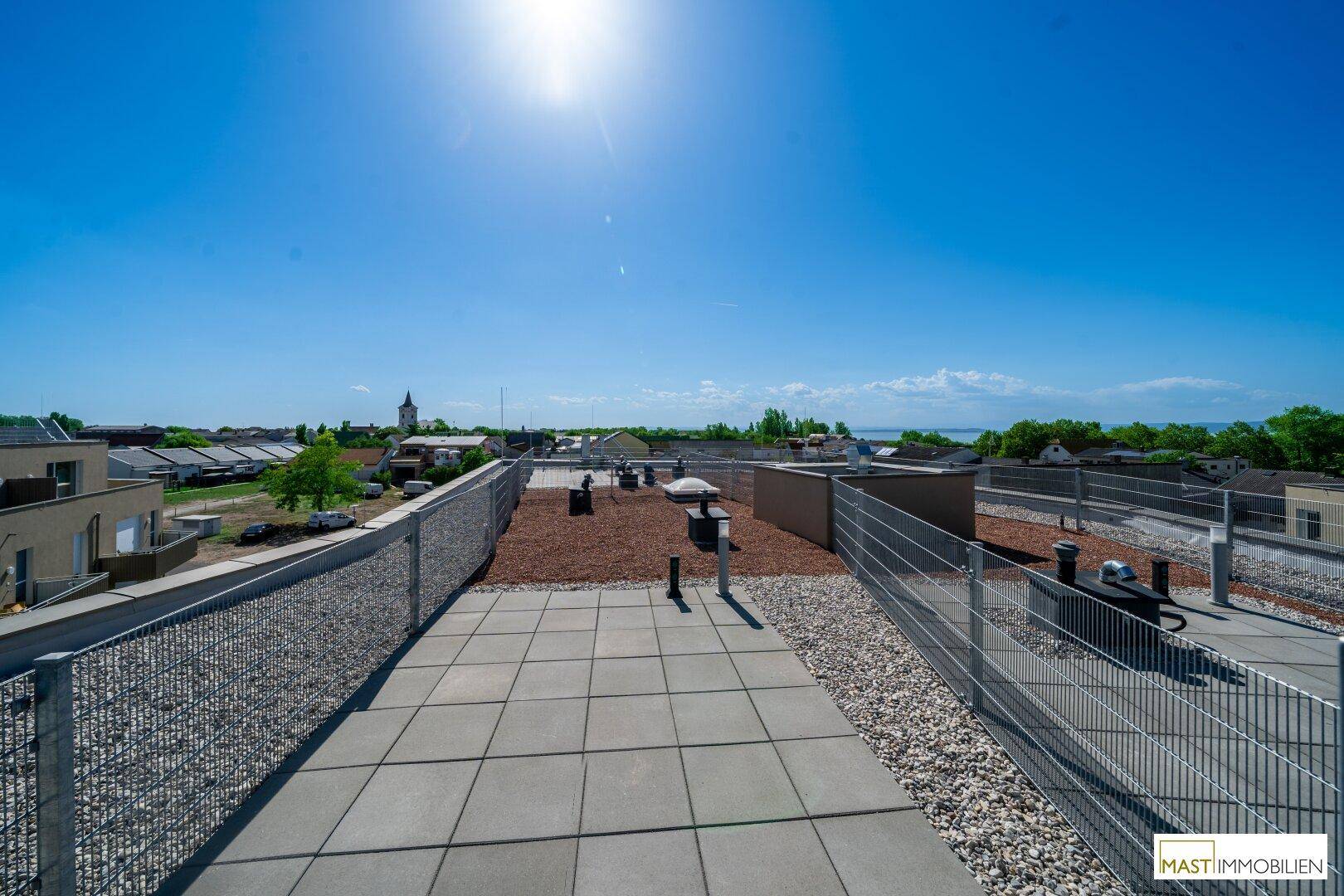 Geräumige Dachterrasse mit Fliesen und Kies, bietet weiten Blick über die Umgebung und einen See.