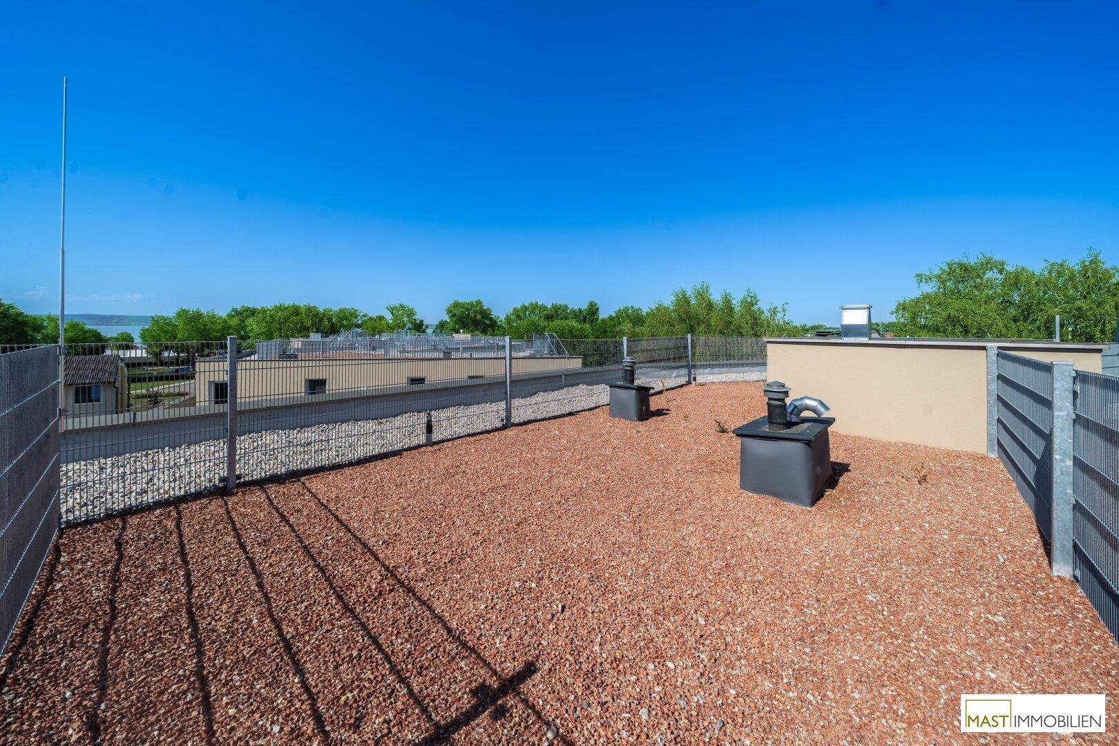 Weitläufige Dachterrasse mit Kiesbelag, umzäunt und mit Fernblick auf das Wasser.