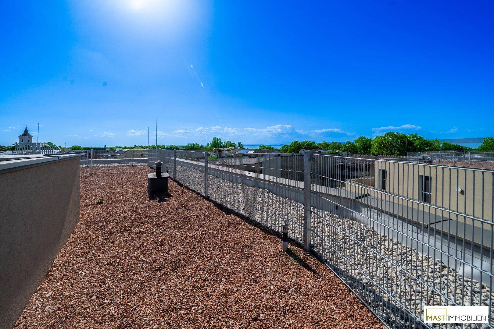 Sonnige Dachterrasse mit Kiesfläche und Panoramablick über die Umgebung und das Wasser.