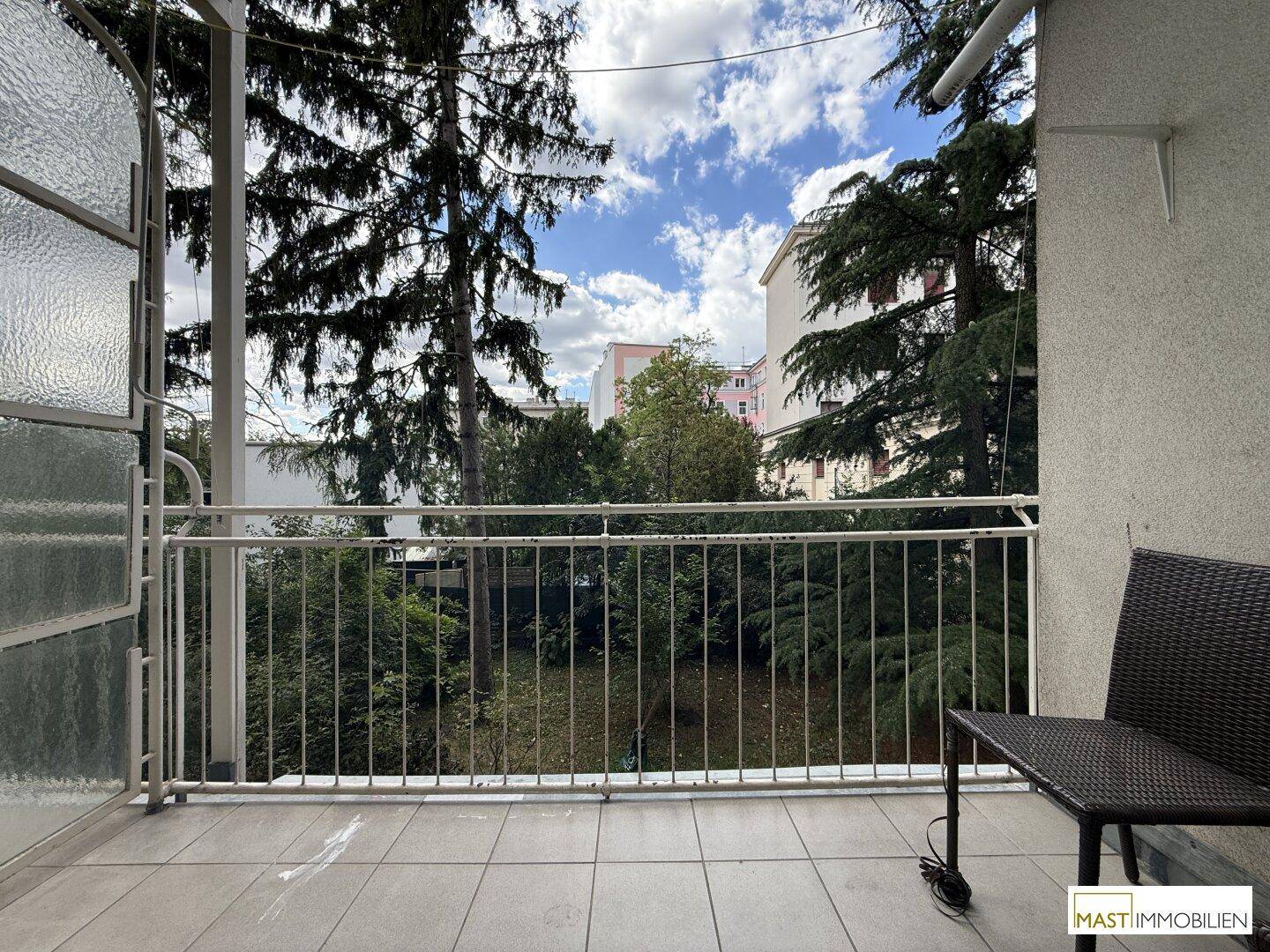 Balkon mit Fliesenboden und Blick ins Grüne sowie auf umliegende Gebäude.