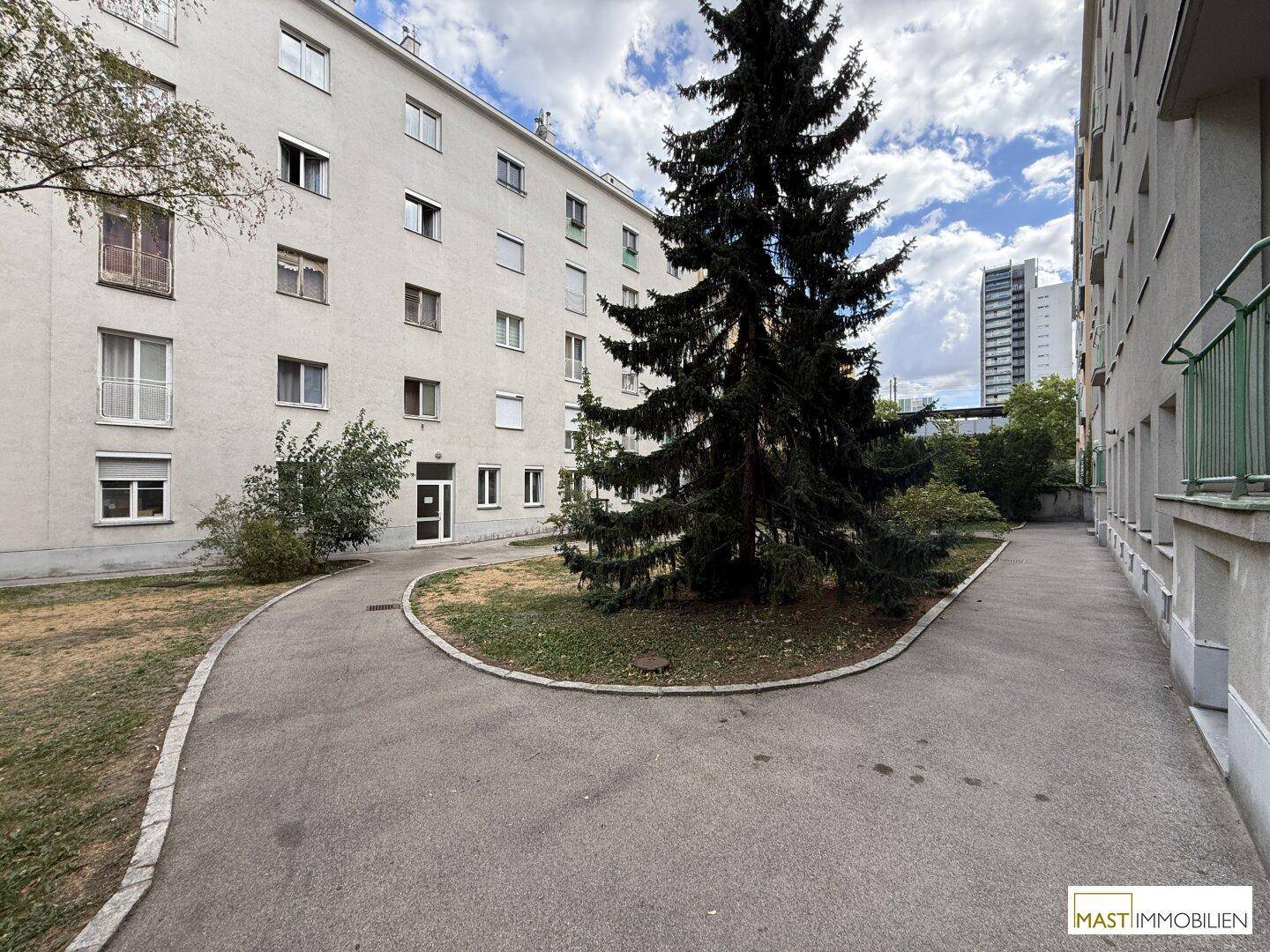 Außenansicht des Wohnkomplexes mit gepflastertem Weg und Grünflächen.