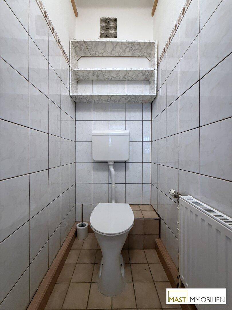 Kleines Gäste-WC mit weißen Fliesen an Wänden und Boden, ausgestattet mit einer Toilette.
