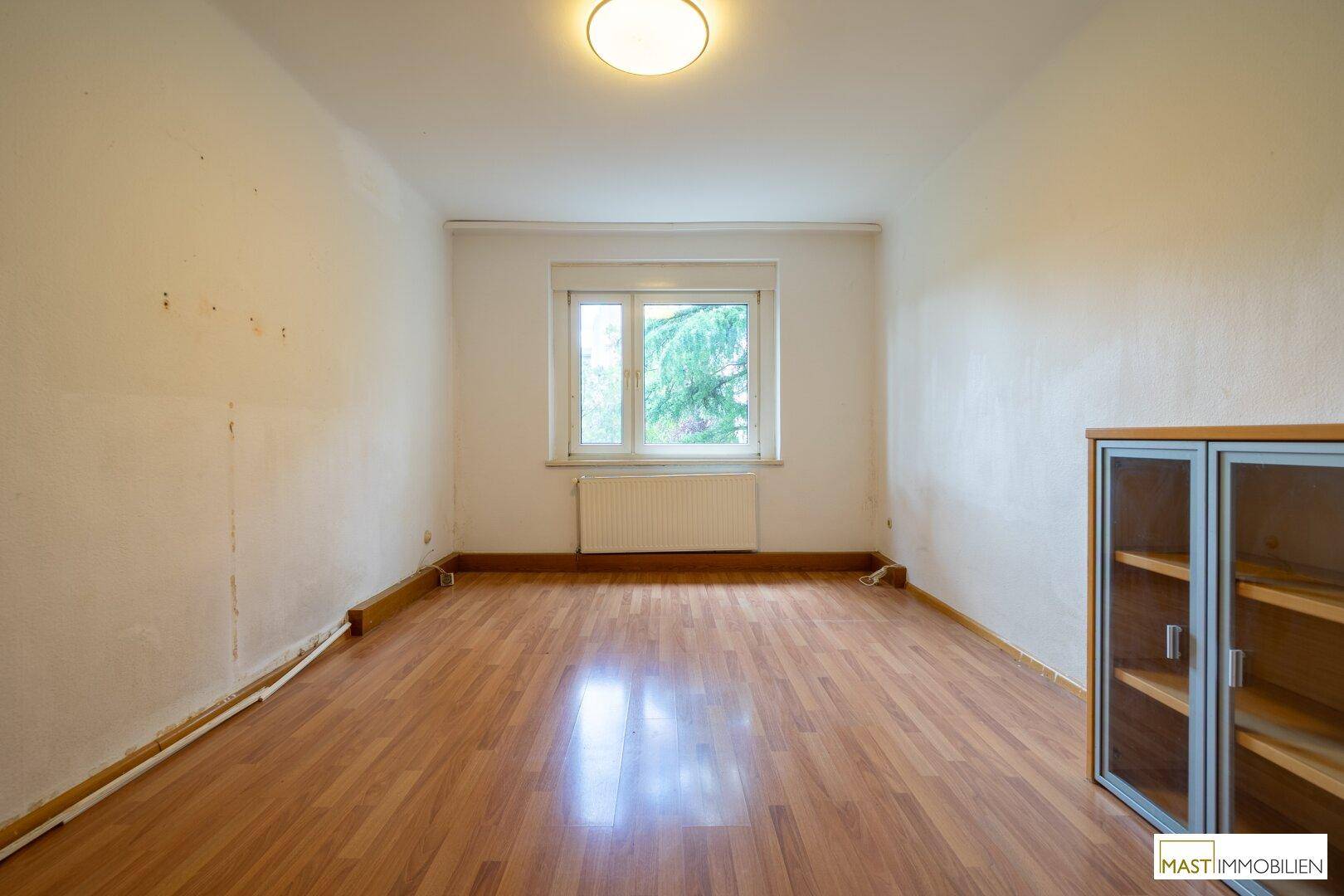 Helles Wohnzimmer mit Laminatboden und Fenster, das viel Tageslicht hereinlässt.