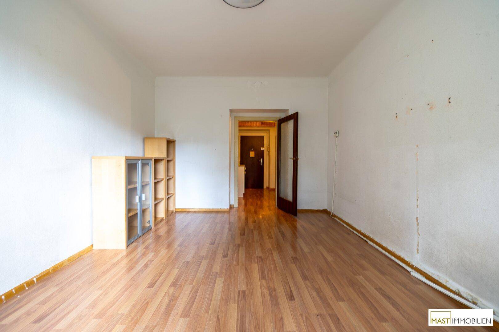 Leeres Wohnzimmer mit Laminatboden und weiß gestrichenen Wänden, bereit zur individuellen Gestaltung.