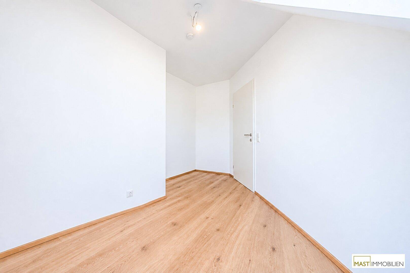 Helles Zimmer mit Holzboden und weiß gestrichenen Wänden, bietet eine ruhige Atmosphäre.