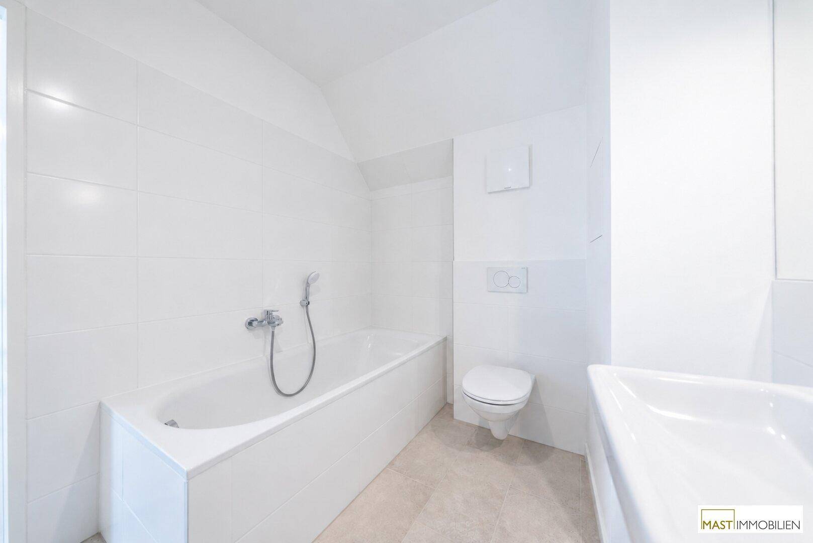 Modernes Badezimmer mit Badewanne, WC und Waschbecken, in hellen Fliesen und weißer Ausstattung.