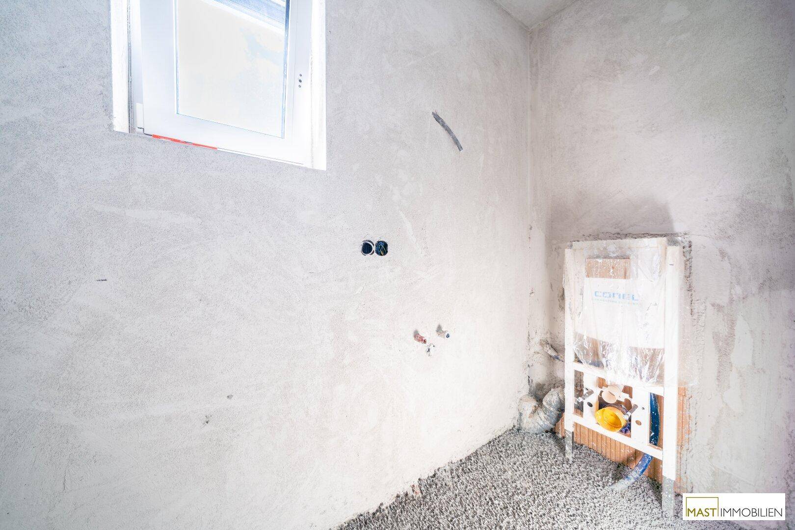 Unfertiges Gäste-WC mit Fenster und vorbereiteter Installation für die Toilette.