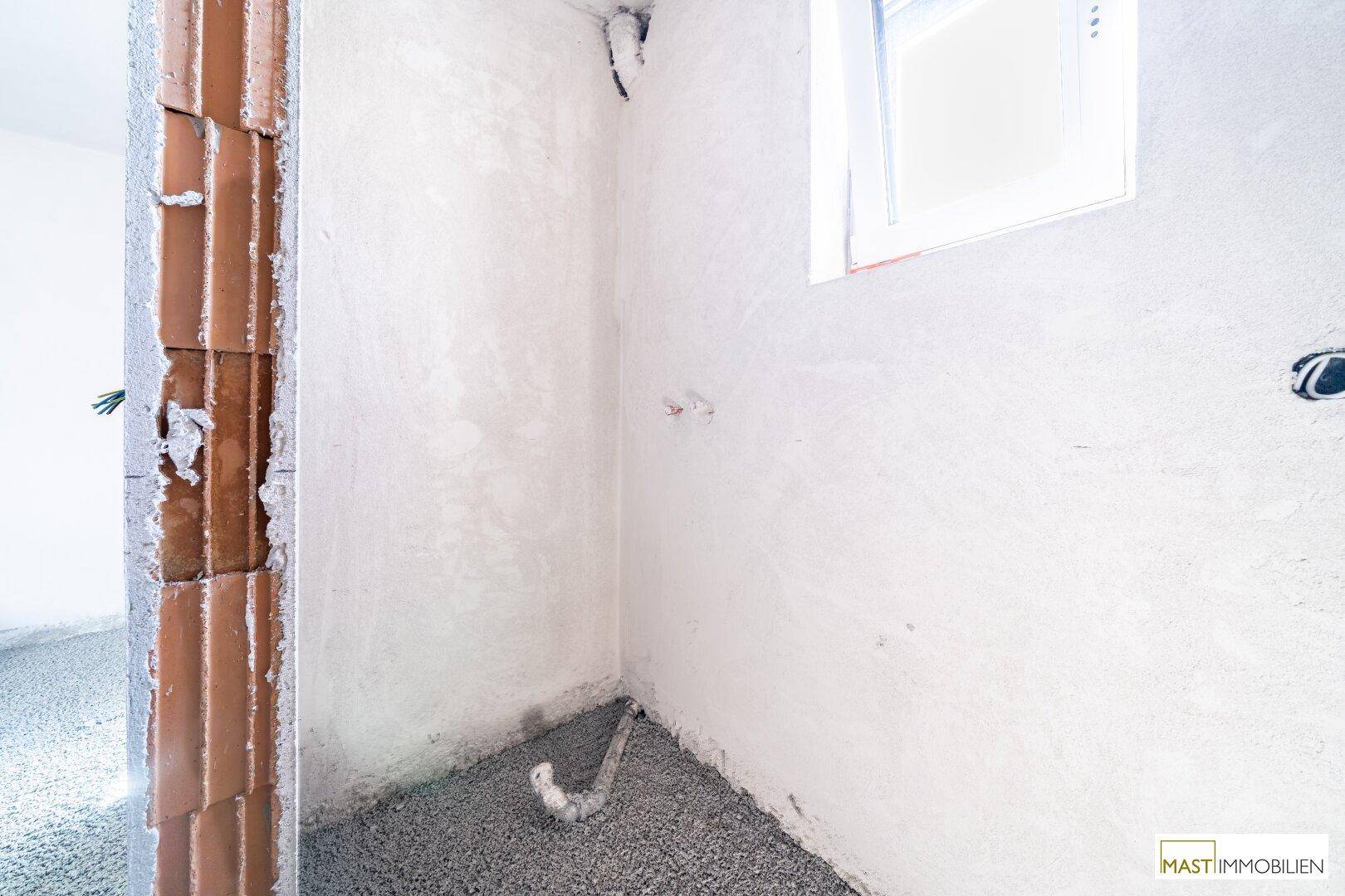 Unfertiger Sanitärraum mit Fenster und sichtbaren Rohinstallationen für Badarmaturen.