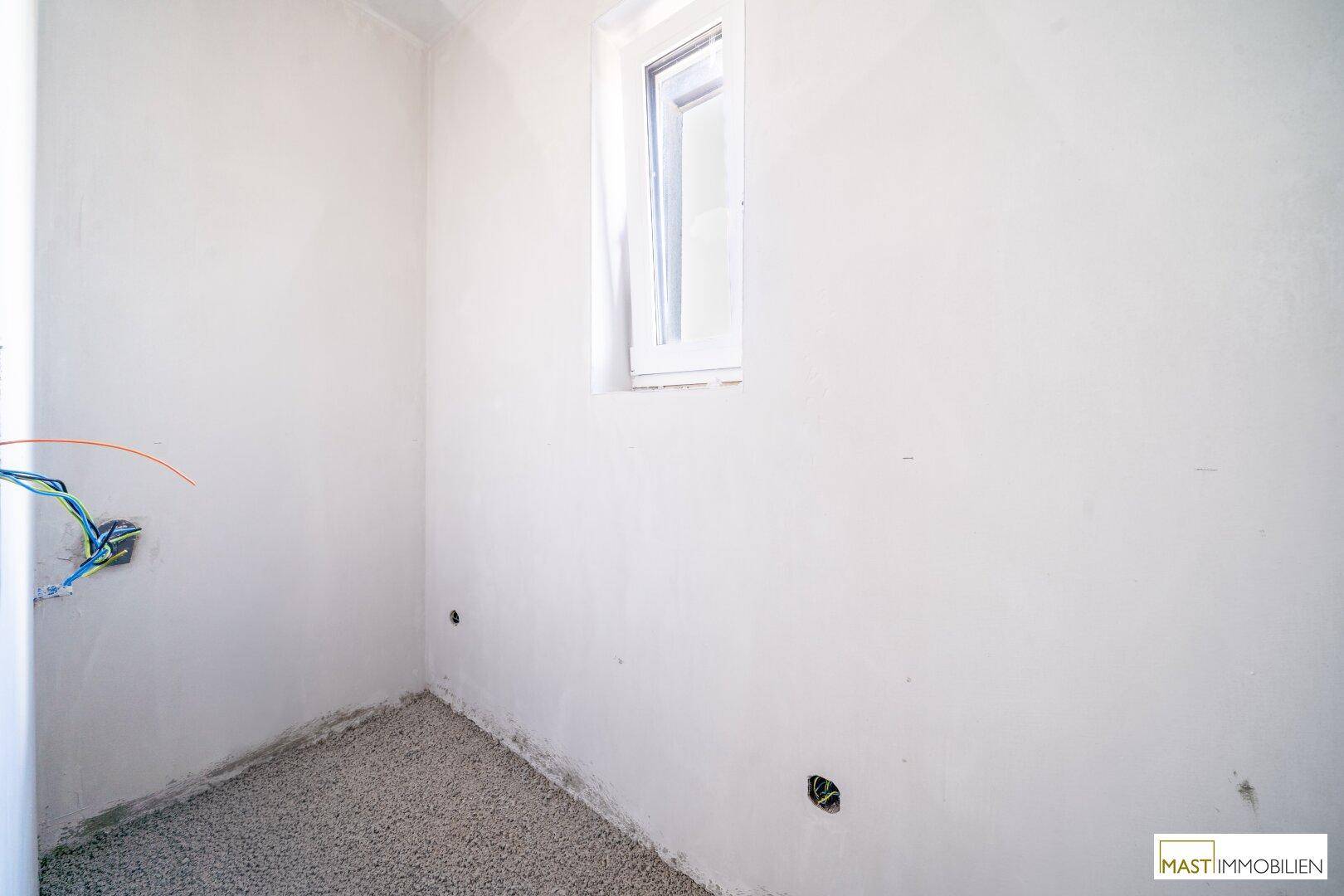 Kleiner, unfertiger Raum mit Fenster und vorbereiteten Elektroinstallationen.