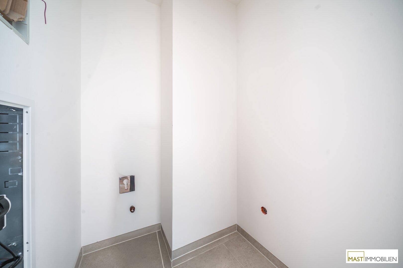 Unfertiger Hauswirtschaftsraum mit Fliesenboden und Anschlüssen, bereit für die Installation.