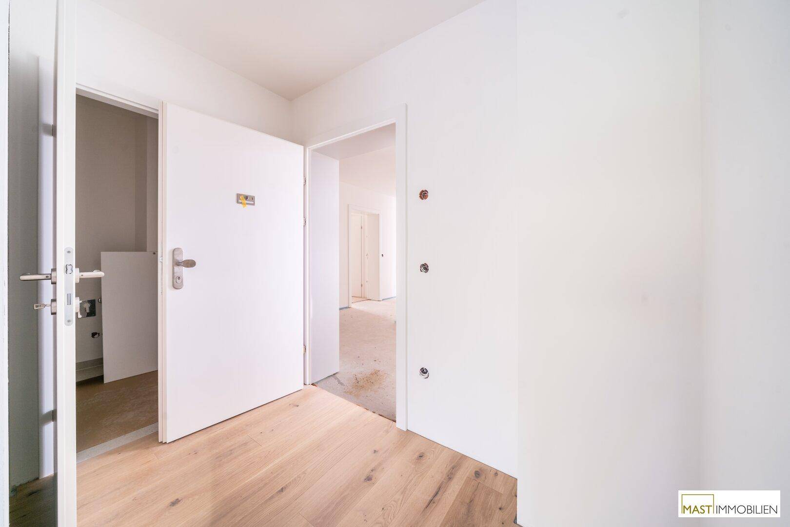 Heller Flurbereich mit Holzboden und mehreren Türen, bereit für den Innenausbau.