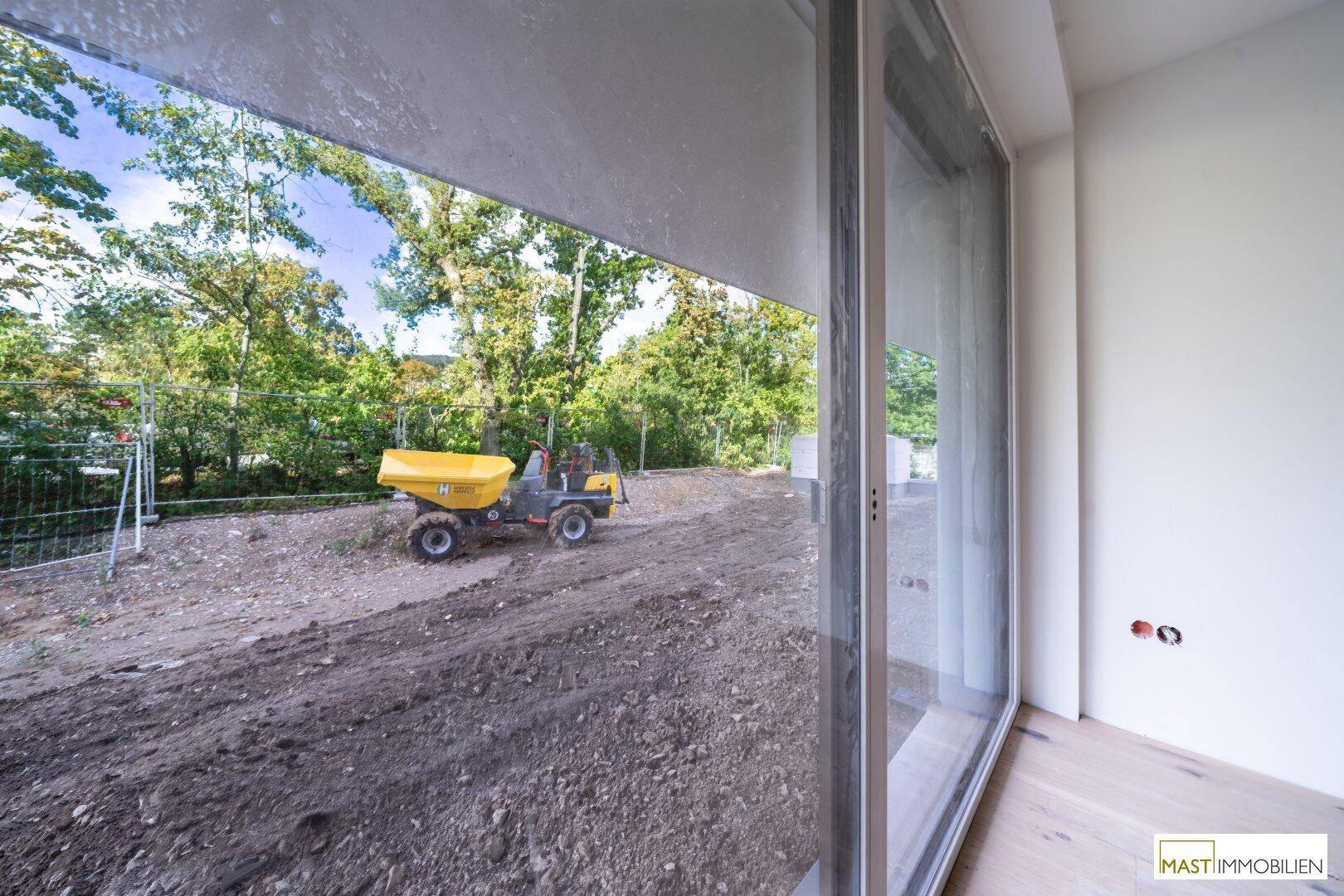 Blick aus dem Fenster auf eine Baustelle mit Bagger und umliegender Natur.