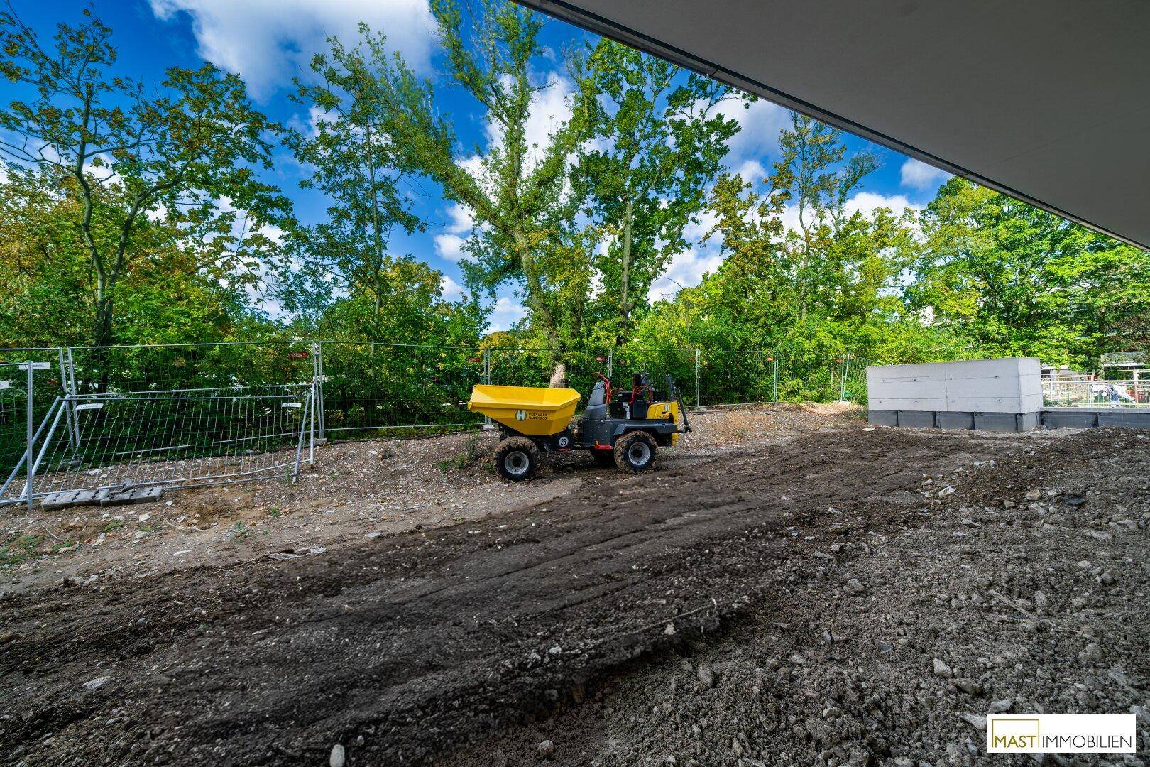 Baustelle im Freien mit einem gelben Dumper und umgebenden Bäumen unter blauem Himmel.