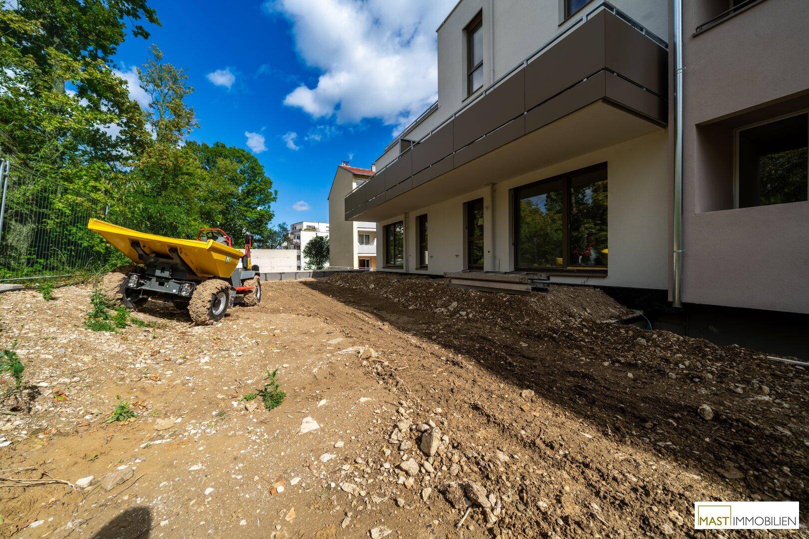Neubau-Fassade mit Balkonen und großen Fenstern, umgeben von einer Baustelle und Bäumen.