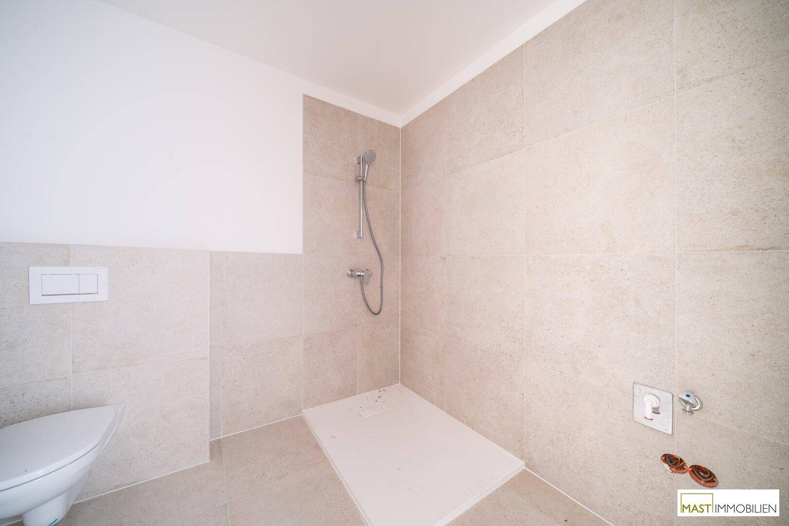 Duschbereich in einem modernen Badezimmer mit hellen Fliesen und Wand-WC.