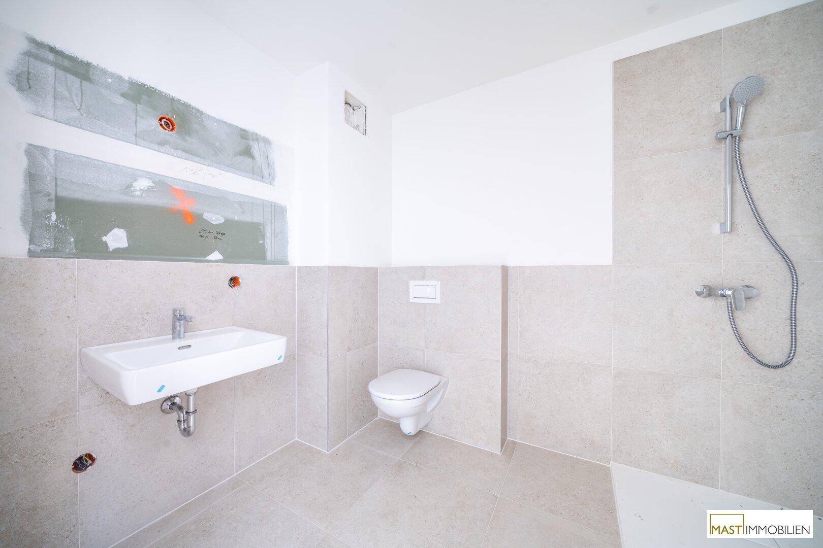 Modernes Badezimmer im Rohbau mit Wand-WC, Waschbecken und Duschbereich.