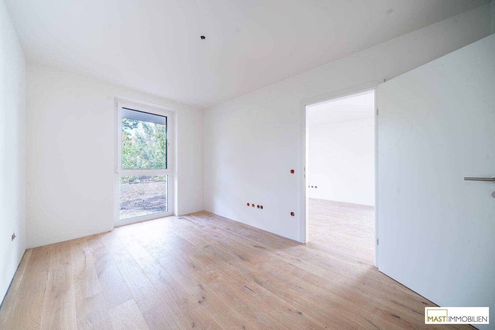 Helles Schlafzimmer mit Holzboden und großem Fenster, bereit für die Einrichtung.