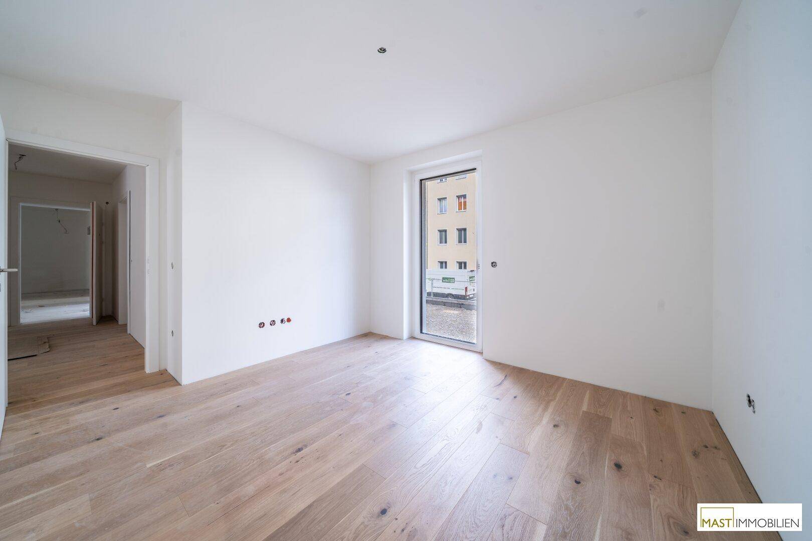 Unmöbliertes Zimmer mit Holzboden und Zugang zu einem Außenbereich, ideal als Schlaf- oder Arbeitszimmer.