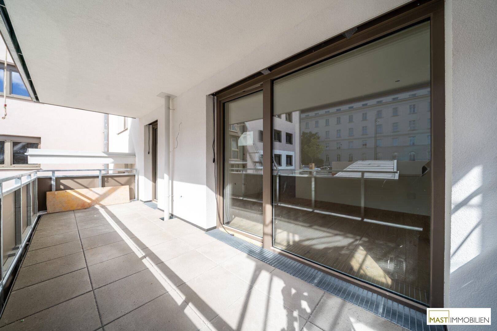 Heller Balkon mit Fliesenboden und großer Glasschiebetür, bietet viel Sonnenlicht und Zugang zum Innenbereich.