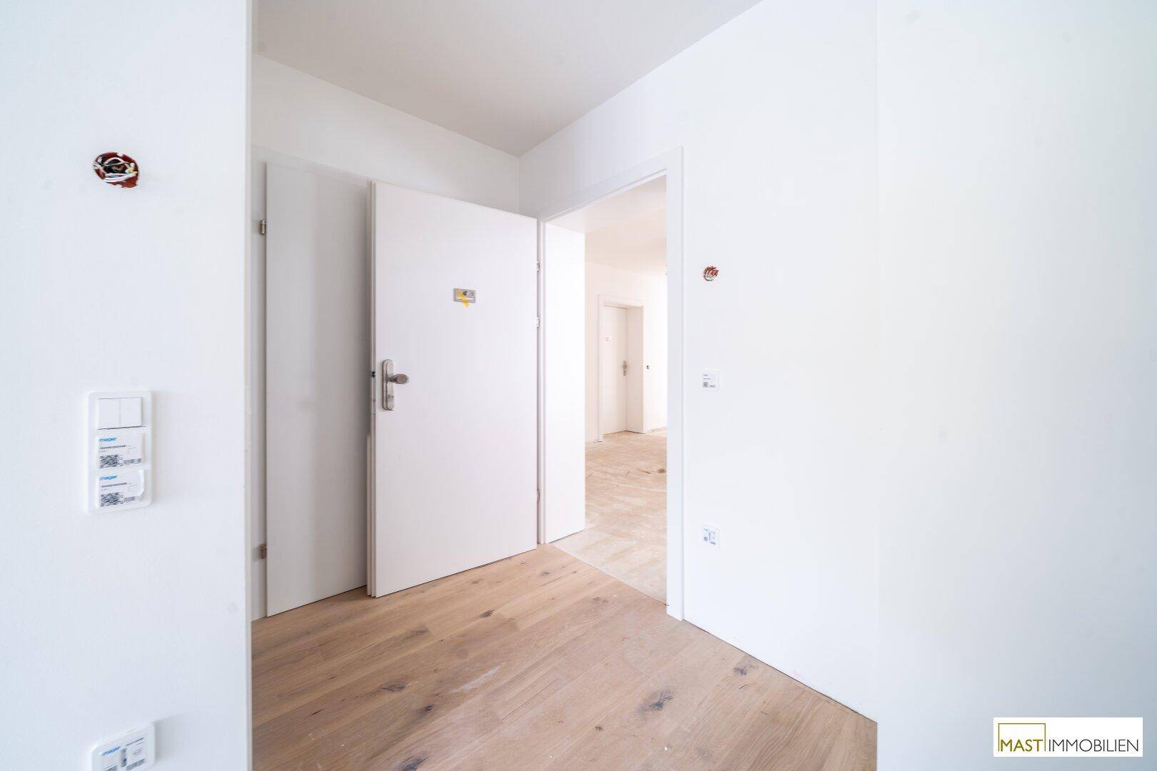 Heller Flur mit Holzboden und weißen Wänden, verbindet verschiedene Räume der Wohnung.