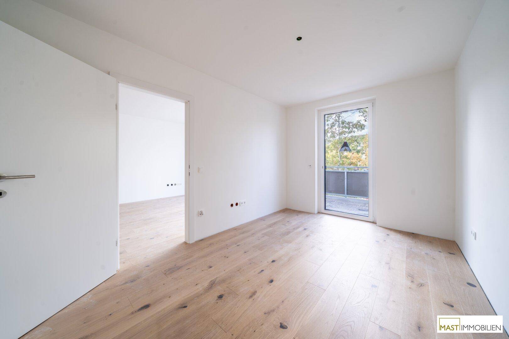 Helles Schlafzimmer mit Holzboden und Zugang zu einem Balkon, ideal für ruhige Nächte.