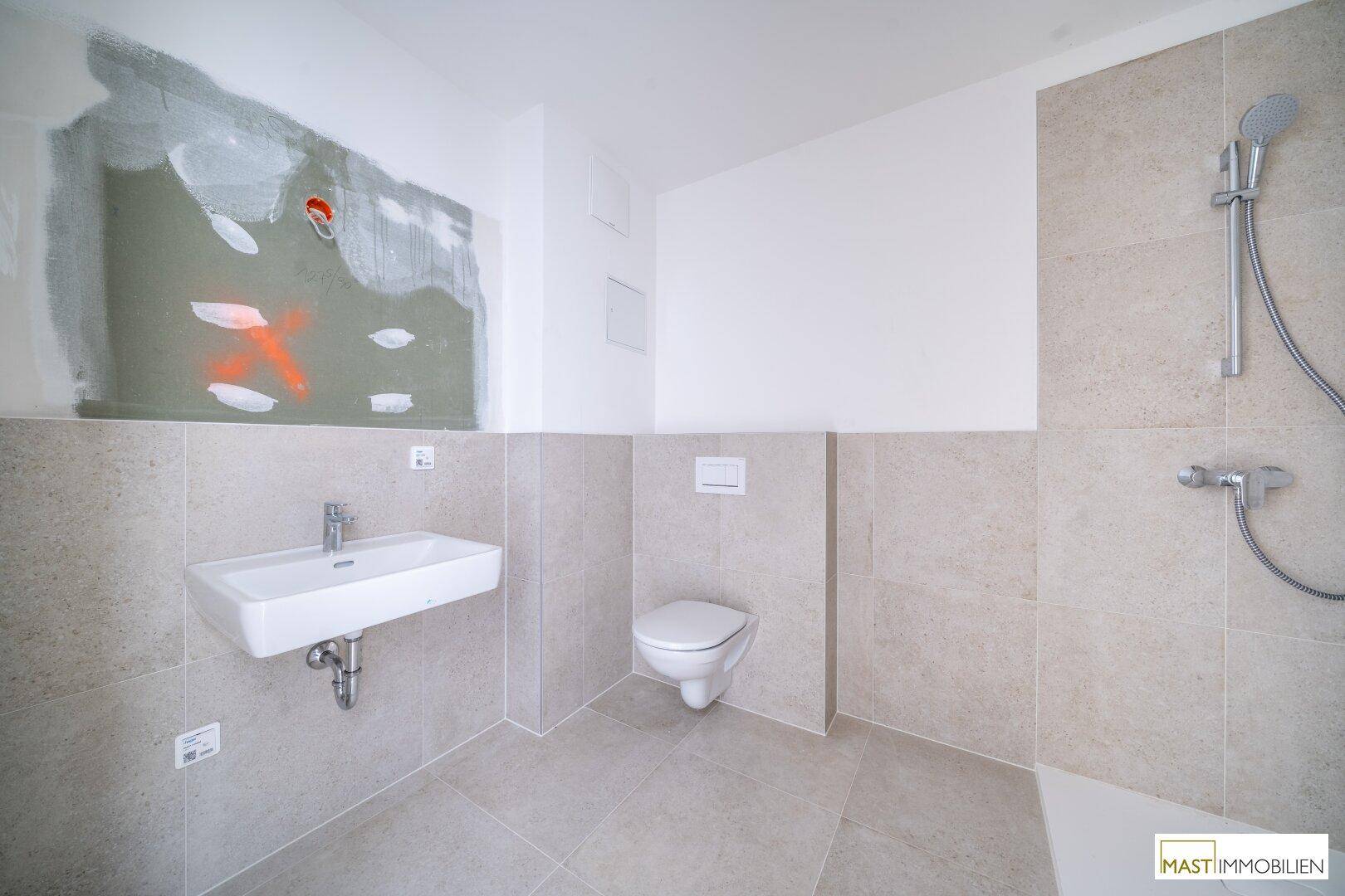 Modernes Badezimmer mit hellen Fliesen, Waschbecken und wandhängendem WC.