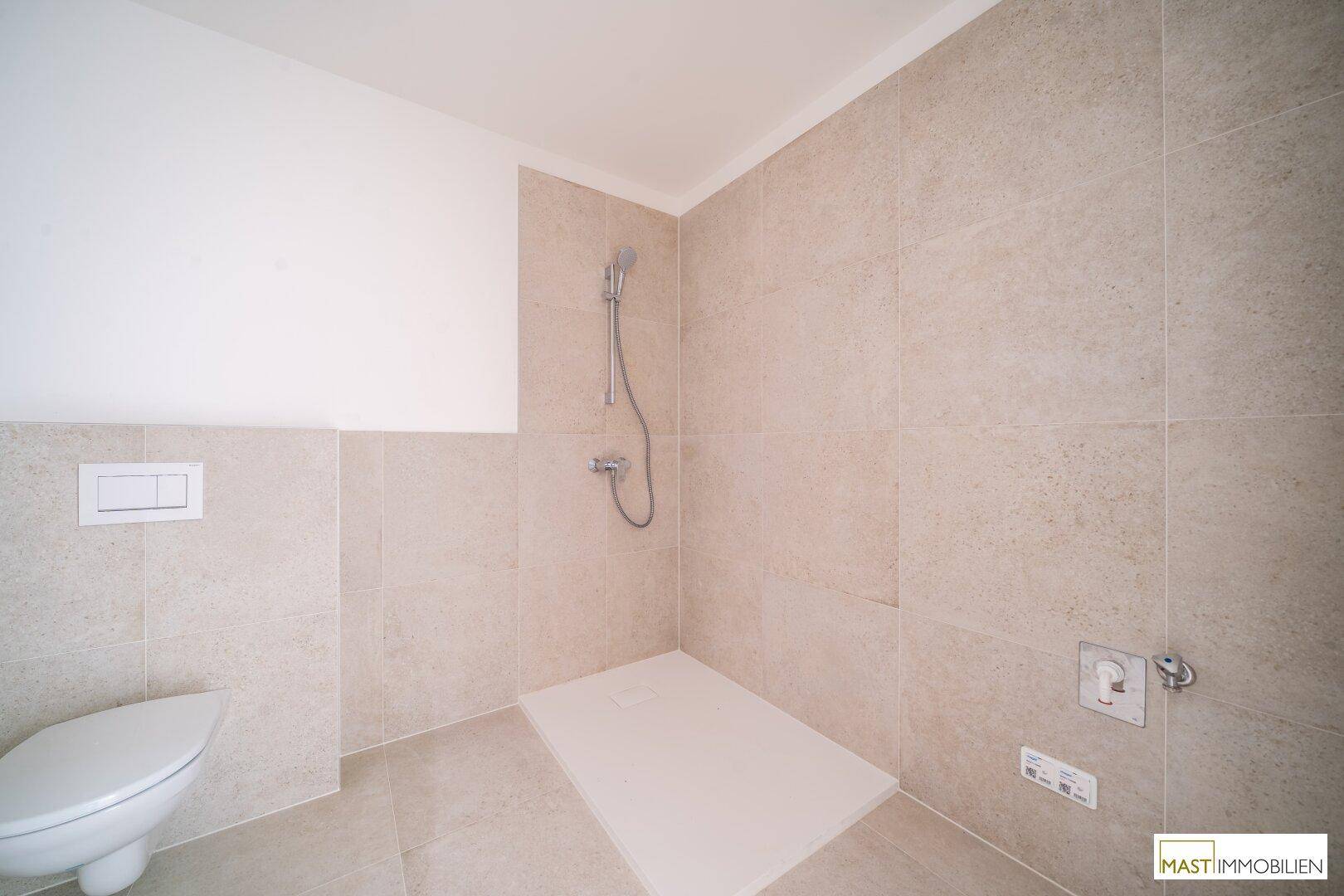 Duschbereich im modernen Badezimmer mit beigefarbenen Fliesen und Duschkopf.