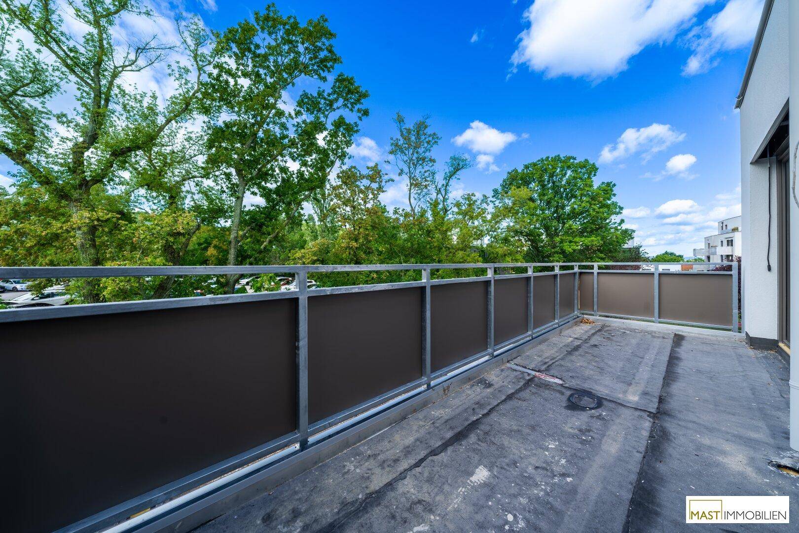 Geräumiger Balkon mit Metallgeländer und Blick ins Grüne.