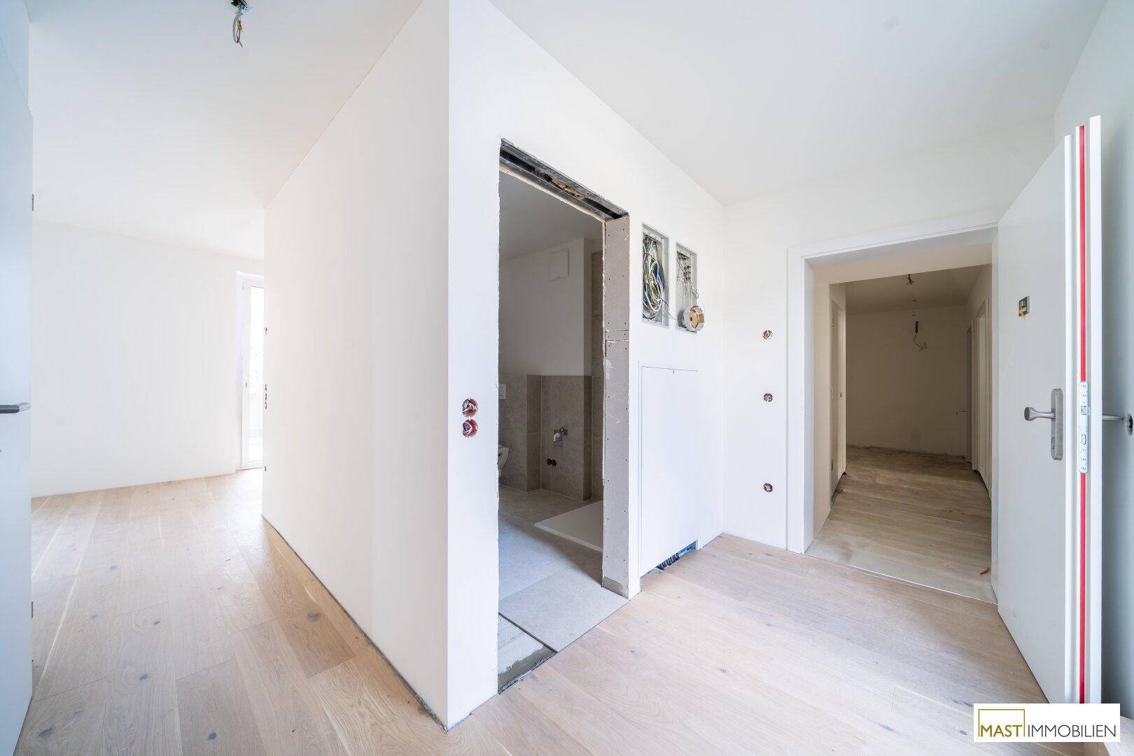 Heller Flur mit Holzboden und mehreren Türen, teilweise im Rohbau.