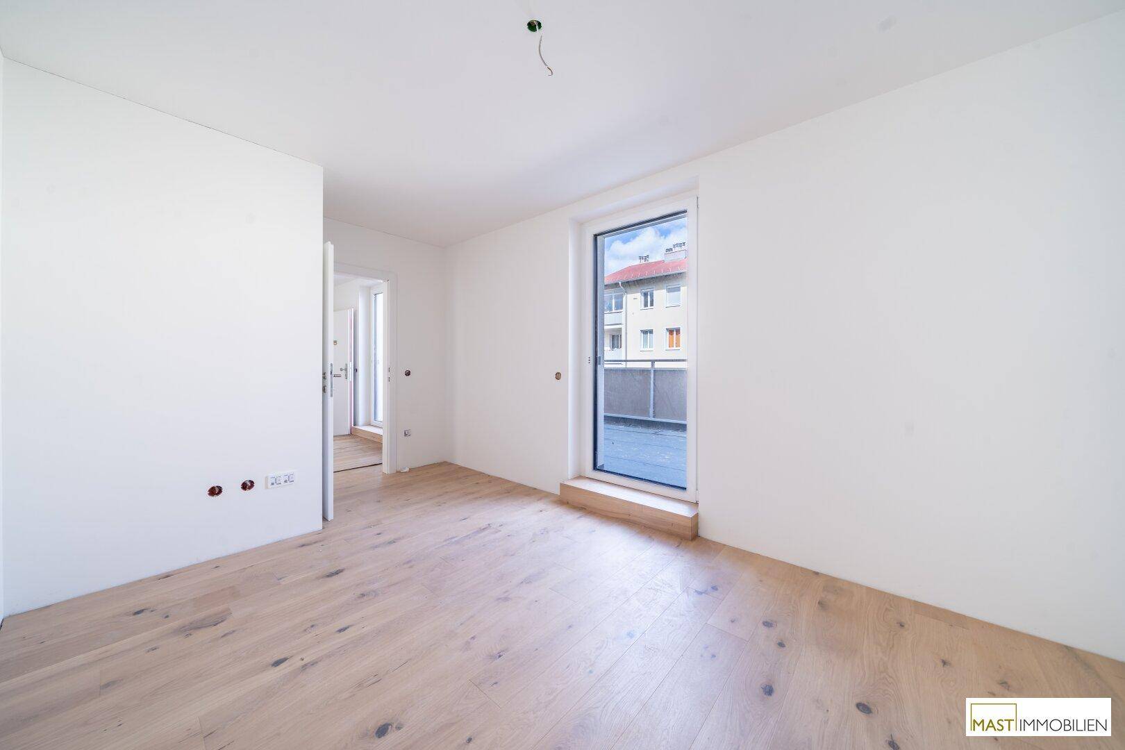 Helles, leeres Zimmer mit Holzboden und großem Fenster mit Stadtblick.