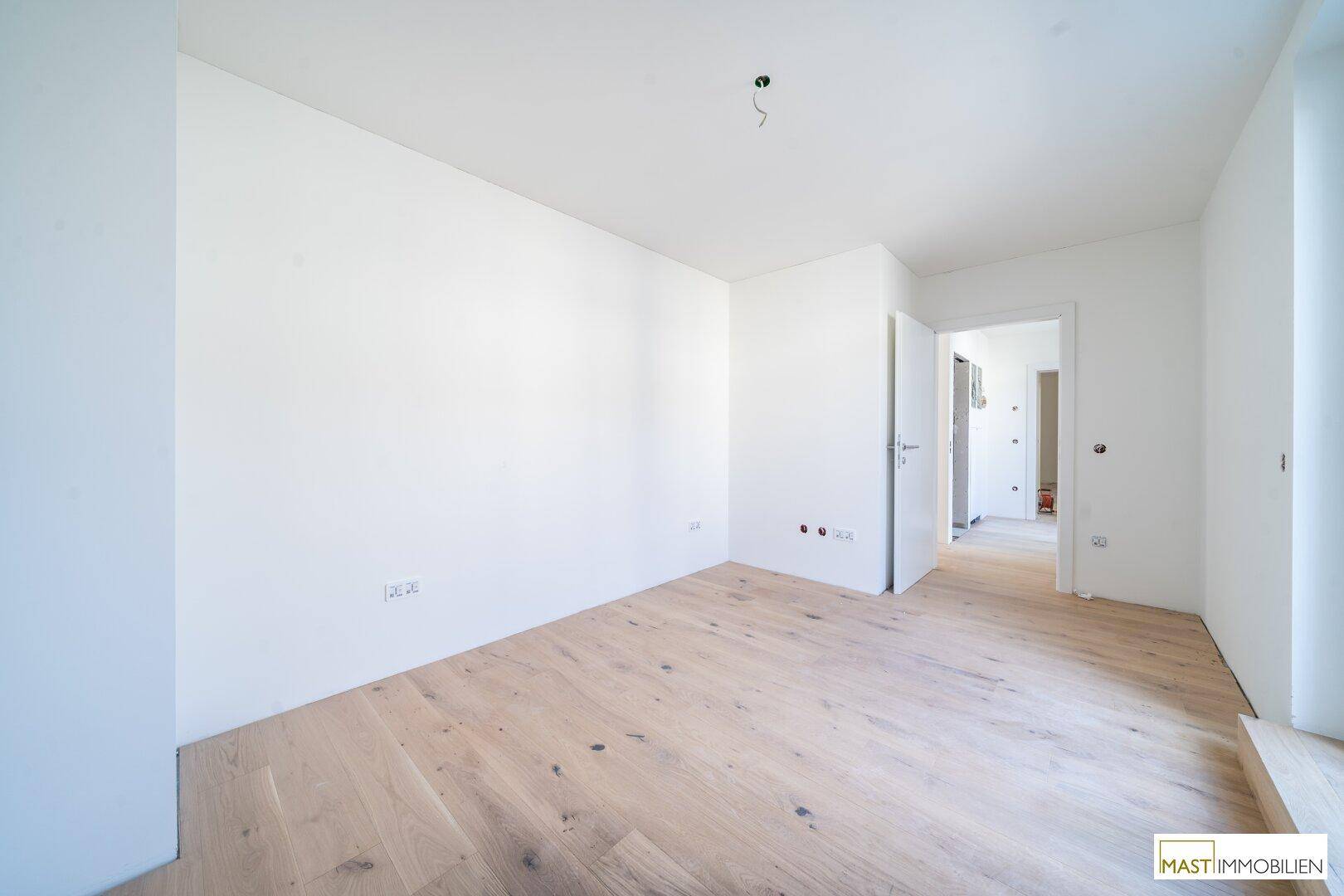 Leeres Zimmer mit Holzboden und weiß gestrichenen Wänden, bereit zur Gestaltung.