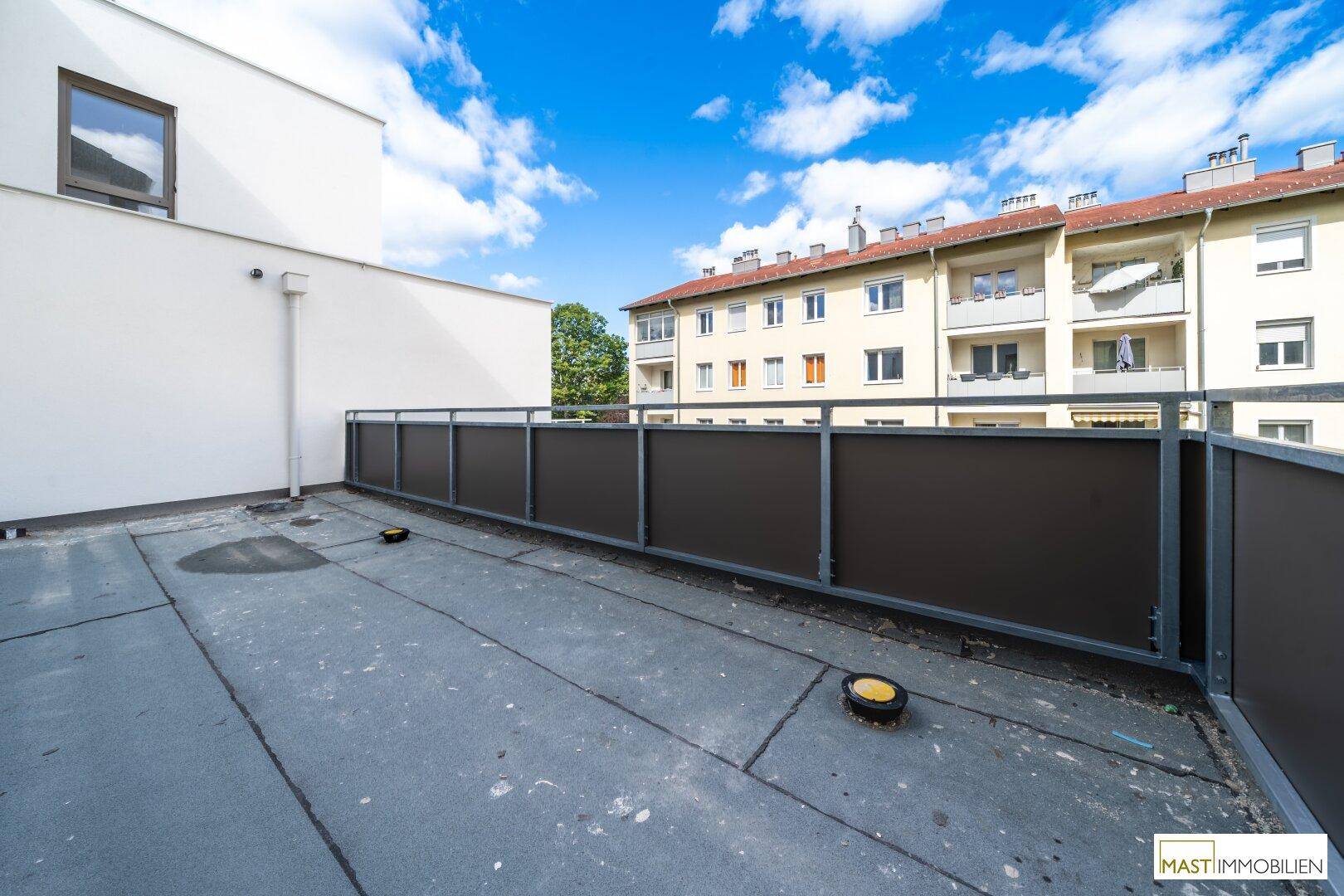 Große, unmöblierte Terrasse mit Blick auf umliegende Gebäude und den Himmel.