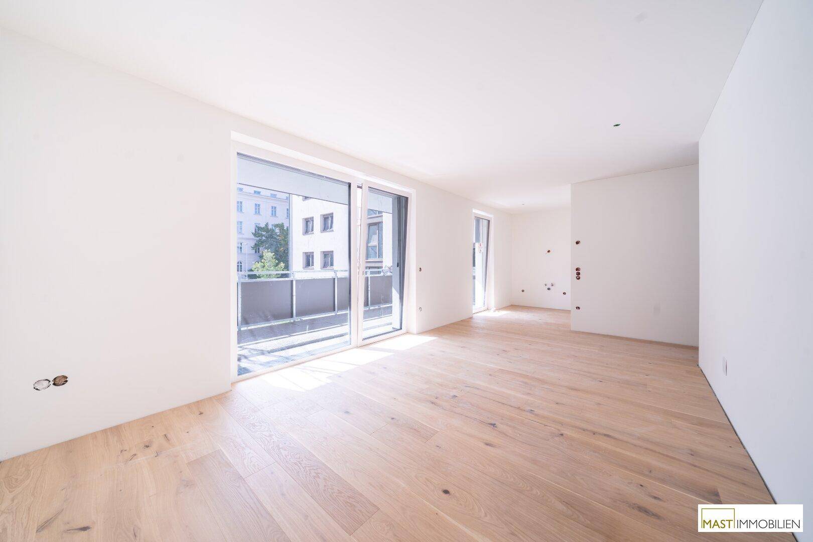 Helles, leeres Zimmer mit Holzboden und Zugang zu einem Balkon.