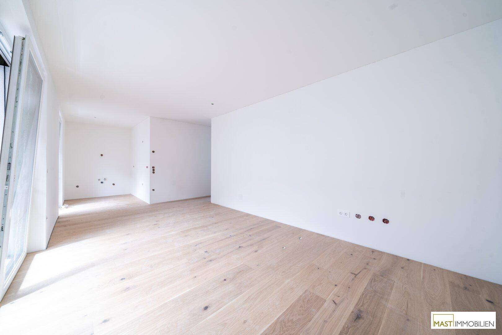 Geräumiges, helles Zimmer mit Holzboden und weißen Wänden, bereit für die Einrichtung.