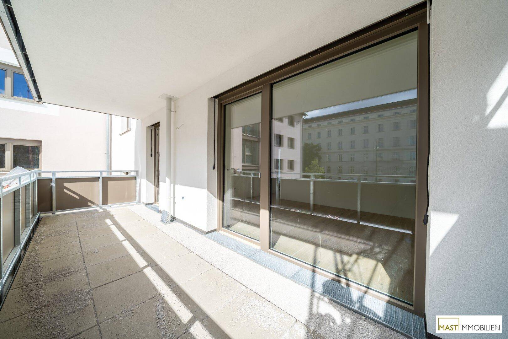 Heller Balkon mit Fliesenboden und großen Schiebetüren zum Innenbereich.