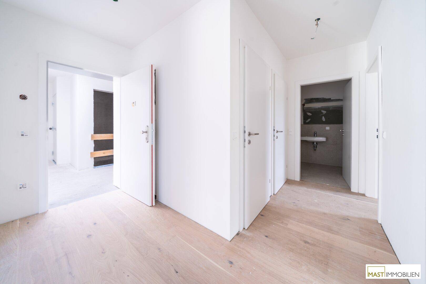 Heller Flur mit Holzboden und mehreren weißen Türen, der zu verschiedenen Räumen führt.