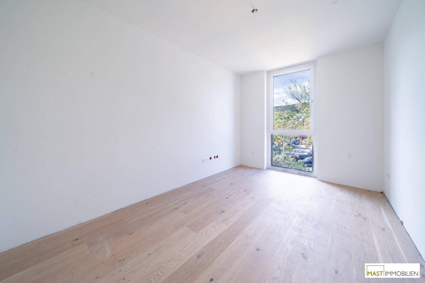 Ruhiges Schlafzimmer mit hellem Holzboden und einem großen Fenster, das viel Tageslicht hereinlässt.