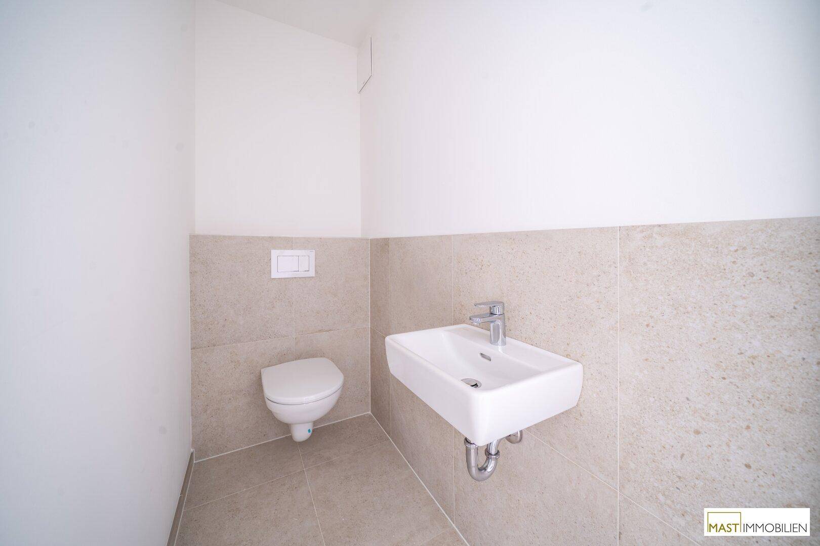 Modernes Gäste-WC mit wandhängender Toilette und kleinem Waschbecken, halbhoch gefliest.