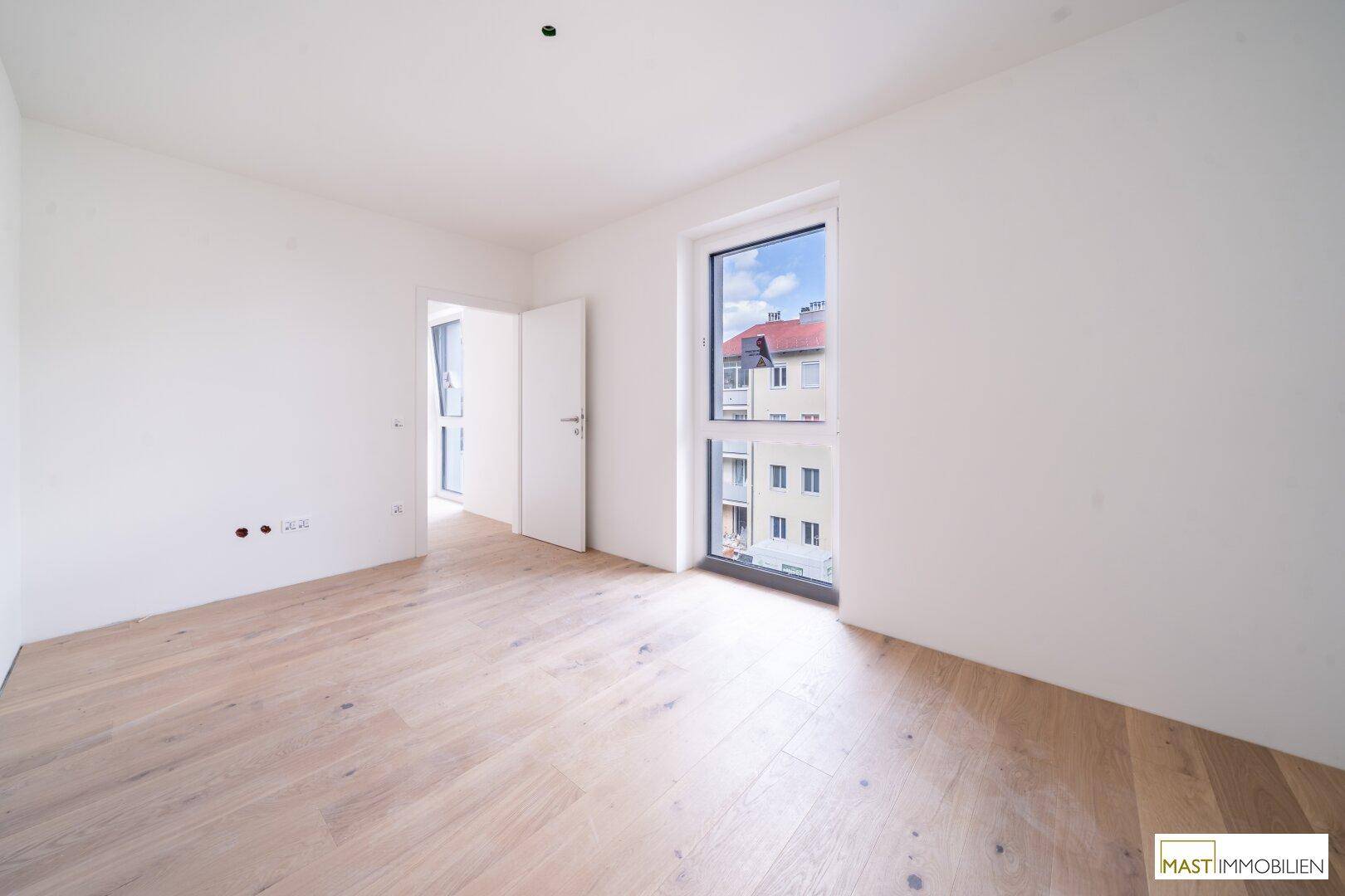 Helles Schlafzimmer mit Holzboden und Fenster mit Blick auf die Stadt.