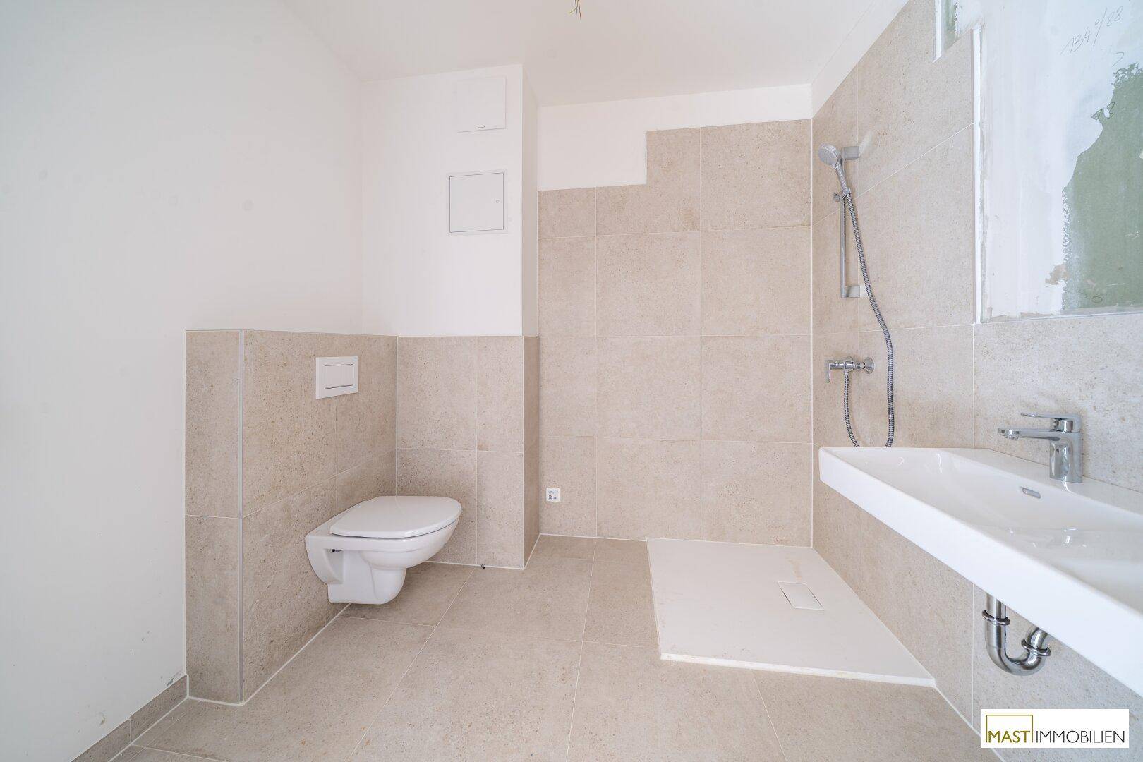 Helles Badezimmer mit beigefarbenen Fliesen, wandhängendem WC und Duschbereich.