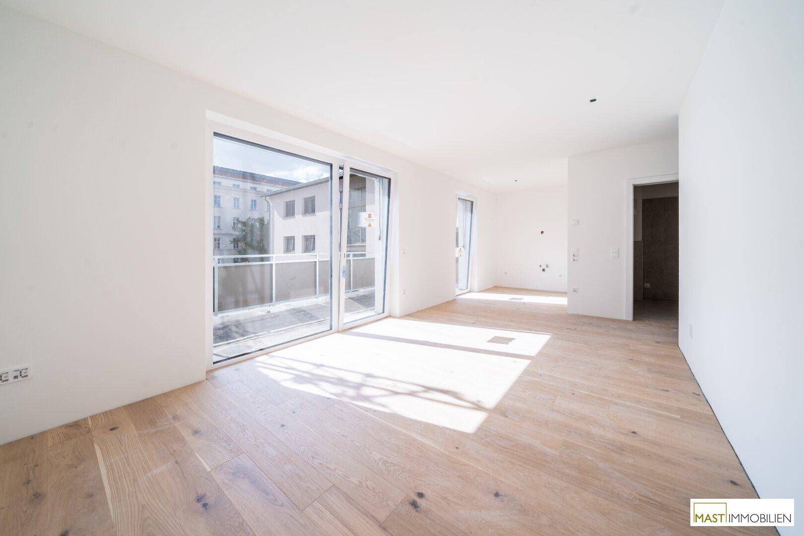 Heller, unmöblierter Raum mit Holzboden und großen Schiebetüren zum Balkon.