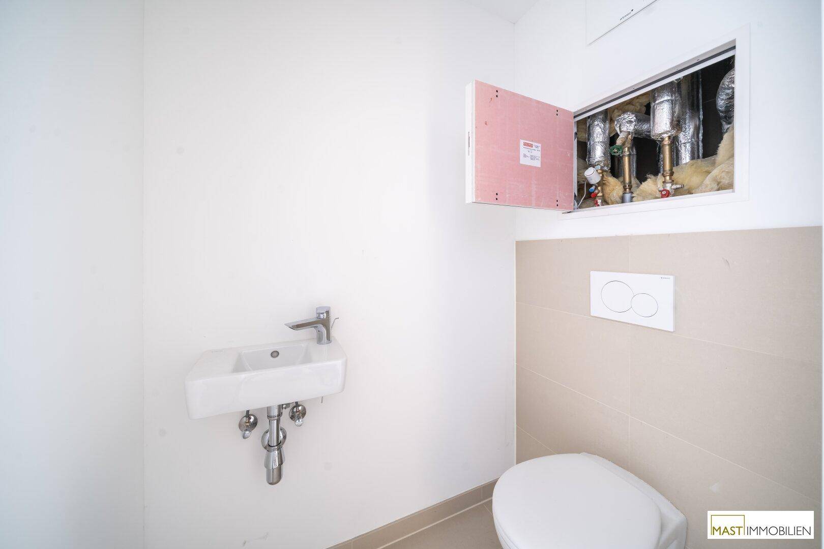 Kompaktes WC mit Waschbecken und wandhängender Toilette, ausgestattet mit beigefarbenen Fliesen.