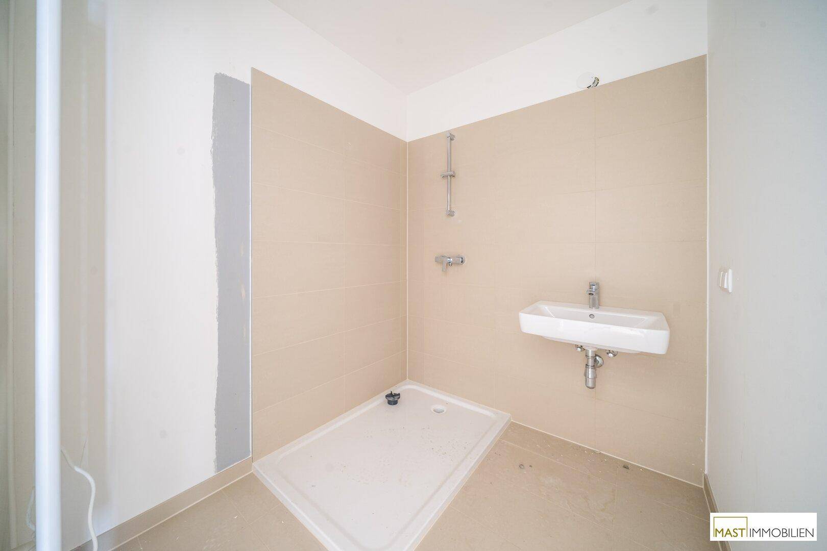 Modernes Badezimmer im Bau mit beigefarbenen Fliesen, Waschbecken und vorbereiteter Duschfläche.