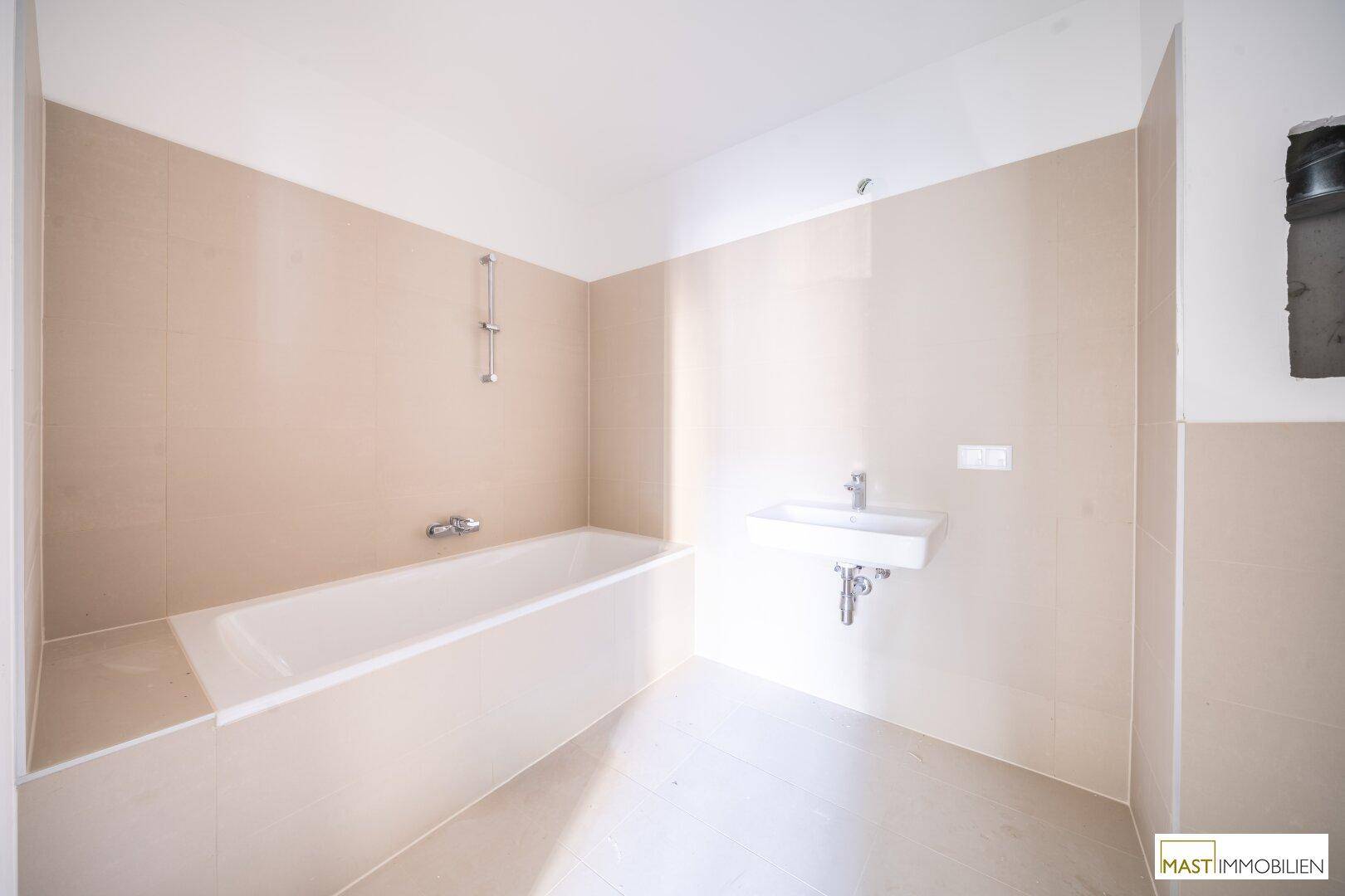 Helles Badezimmer im Bau mit beigefarbenen Fliesen, Waschbecken und einer eingebauten Badewanne.