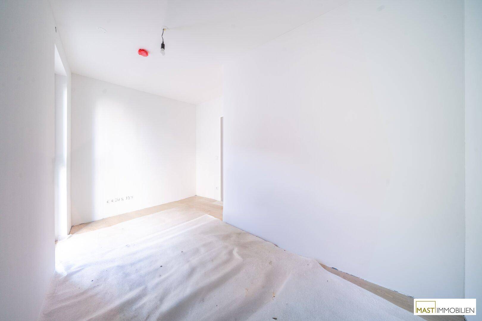 Unmöbliertes Zimmer mit weiß gestrichenen Wänden und geschütztem Boden, profitiert von viel natürlichem Licht.