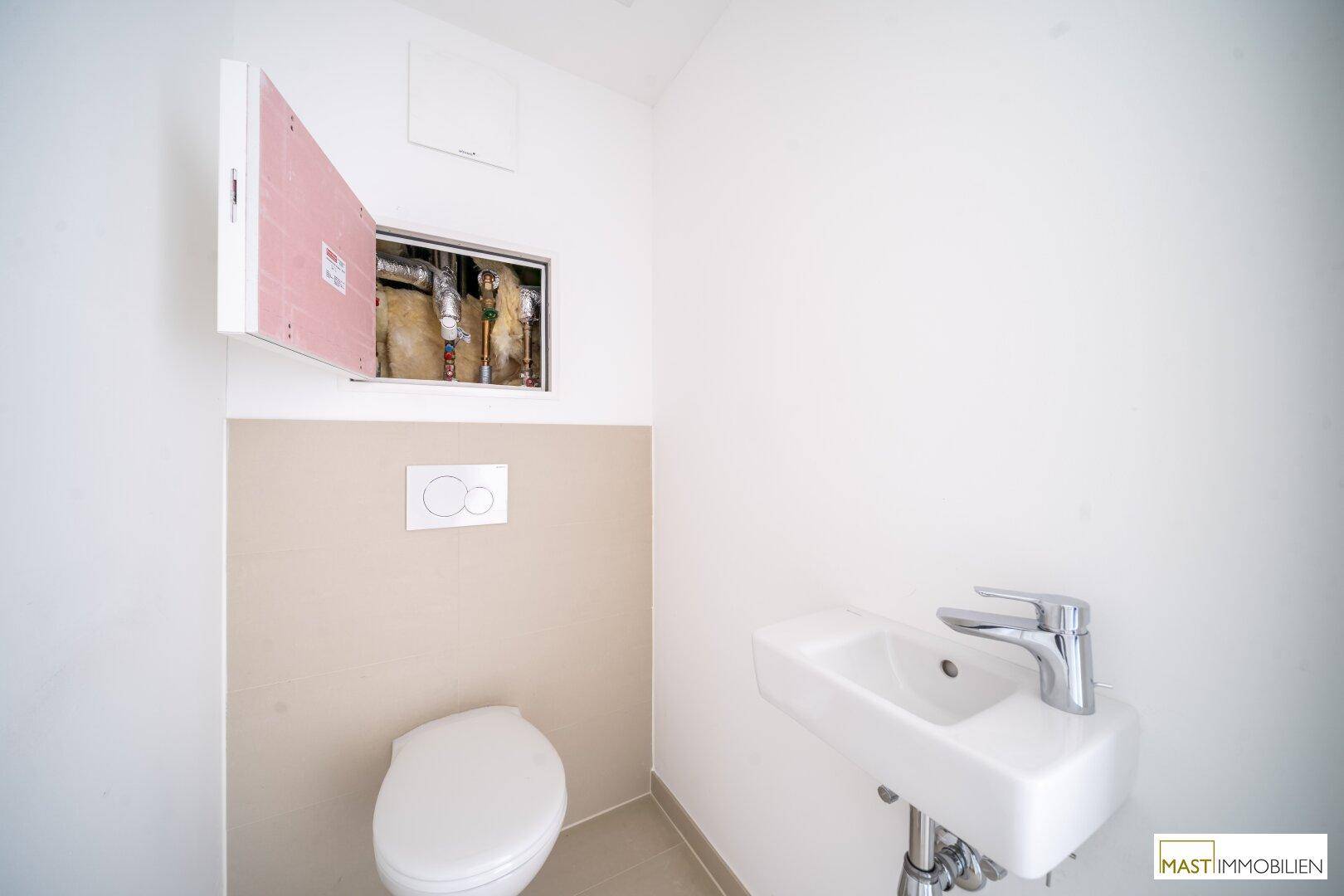 Modernes Gäste-WC mit wandhängender Toilette, kleinem Waschbecken und beigefarbenen Fliesen.